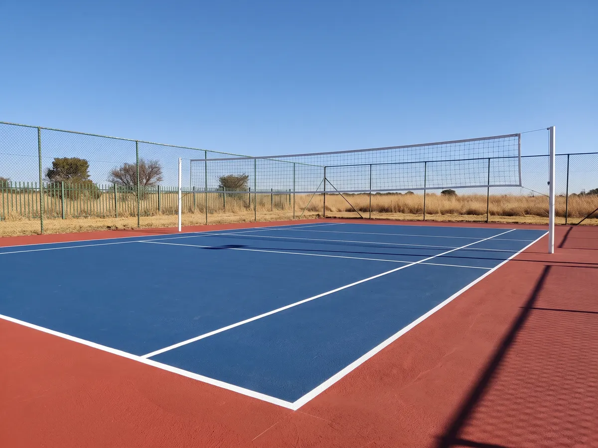 Newly coated blue and red hard-surface outdoor volleyball court with white line markings and net
